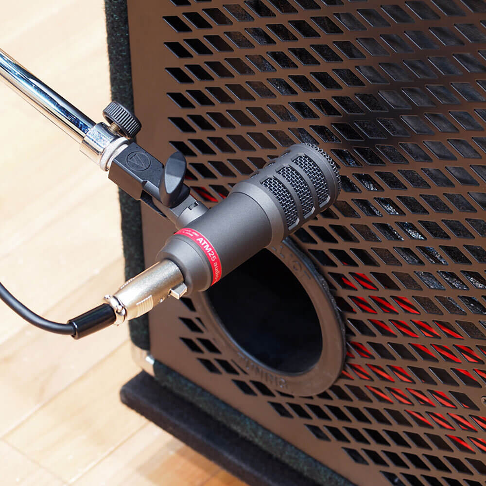 Audio-Technica ATM25 - Hypercardioid Dynamic Instrument Microphone with an integral stand clamp, mounted in front of a base cabinet