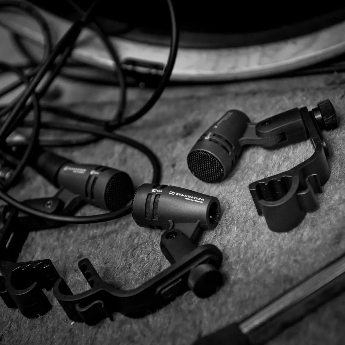 Sennheiser 3-PACK e 604 Dynamic Cardioid Instrument Microphone Set with mounting clips arranged on a textured gray surface in a monochrome photograph.